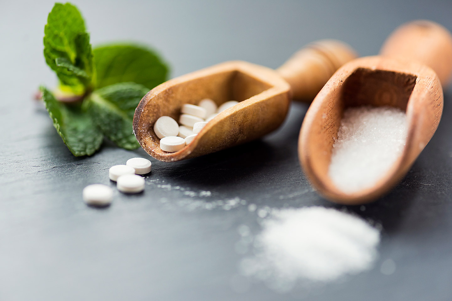 Holzlöffel mit Xylit und Tabletten sowie frische Minze – Symbolbild für Xylit-Vergiftung.